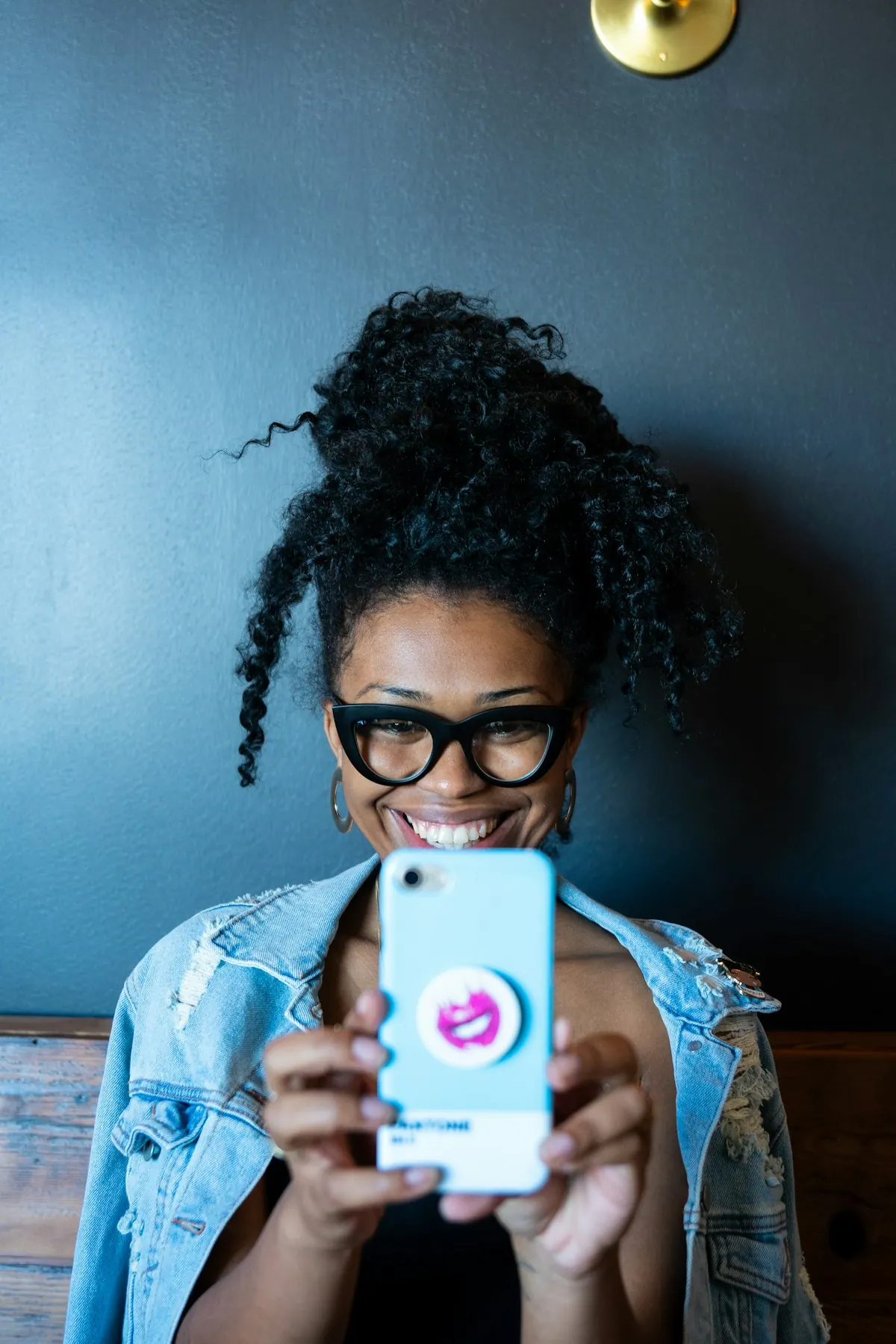 A young woman with glasses smiling while filming herself on her phone